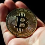 Main dans l'ombre tenant un Bitcoin brillant.