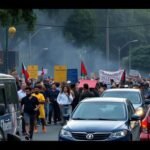 Manifestation dans la rue avec une foule et des véhicules arrêtés.
