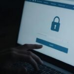 Main de pirate informatique sur un clavier devant un écran